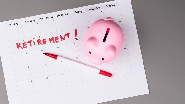 A sheet of paper with the month printed out on it, retirement written on it, and a red pen and pink piggy bank on top.