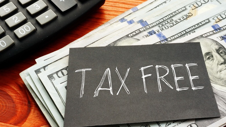 A small black sign that says, "TAX FREE" on it with a stack of hundred dollar bills and a calculator in the background.