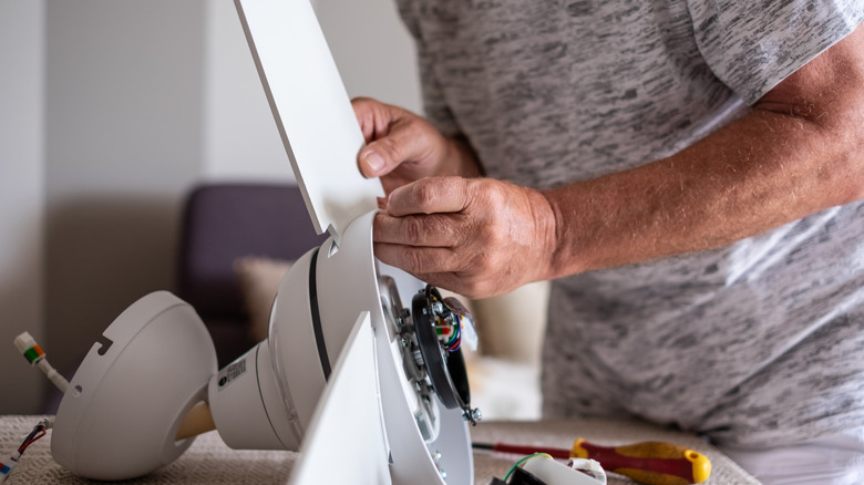 A man dismantling a white ceiling fan.