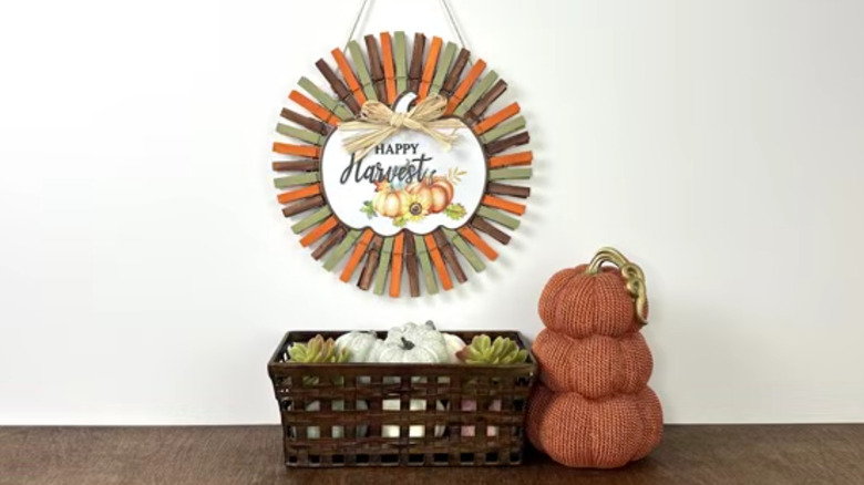 A DIY wreath made of clothespins hangs on the wall above a countertop display of pumpkins in a basket.