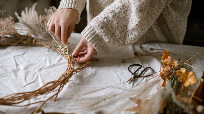 Hands making a fall wreath on a table full of rustic crafting supplies.