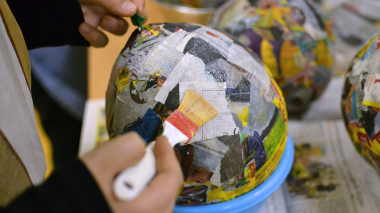 Hands gluing newspaper strips to a balloon for a paper mache craft