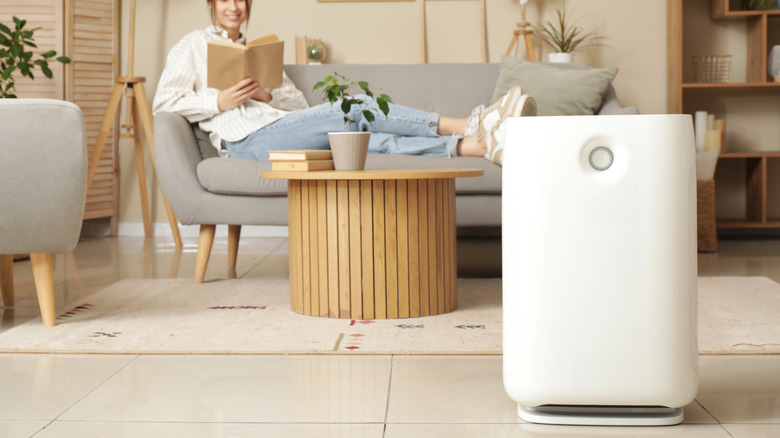 A humidifier is on the floor as a young woman sits on a sofa