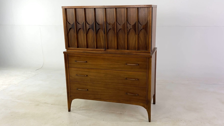 A midcentury modern chest in dark wood on a white background.