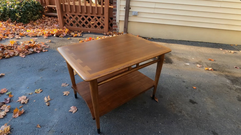 An antique Lane furniture piece with geometric inlays, sitting on a driveway during the fall.