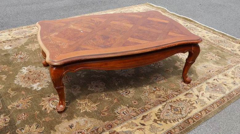 An antique Thomasville coffee table with an inlay sitting on a rug outside.