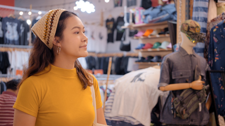 young asian woman in second hand clothing store wearing a yellow shirt and knitted hat