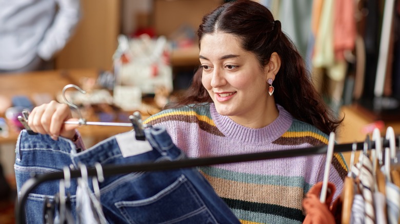 young woman examining a pair of jeans on a hanger at a thrift shop