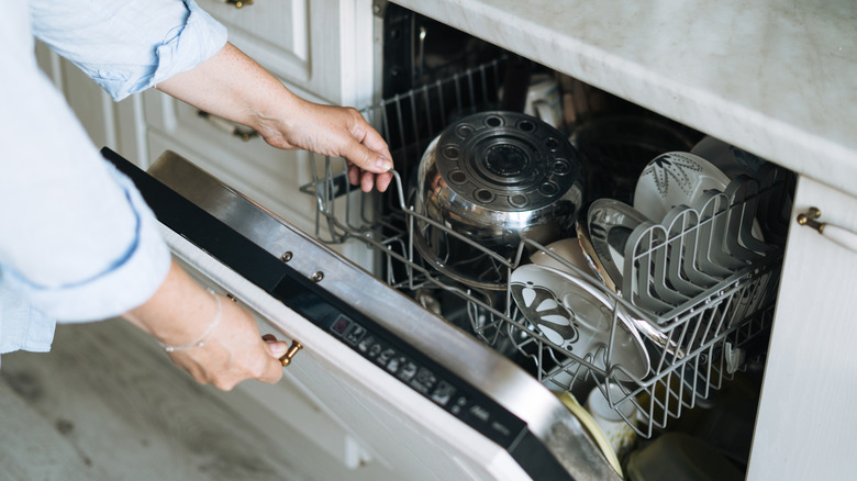 person closing dishwasher loaded with dishware