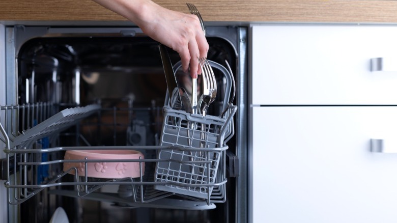 person putting fork in utensil basket of compact dishwasher
