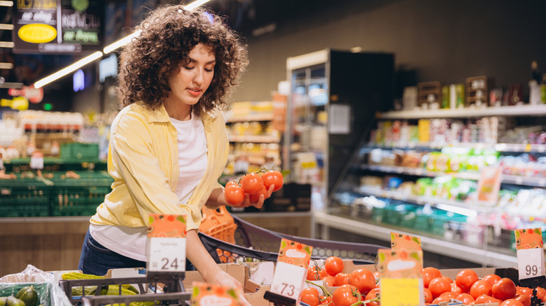 A dark-haired woman shops for tomatoes at the supermarket.