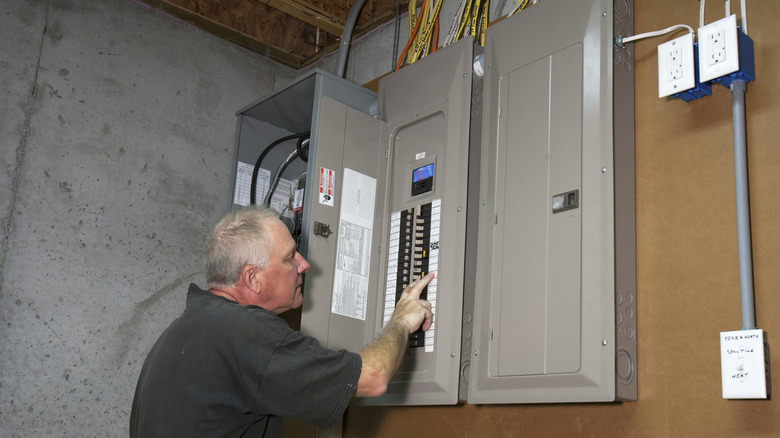 Man inspects electrical circuit breaker box with the door open