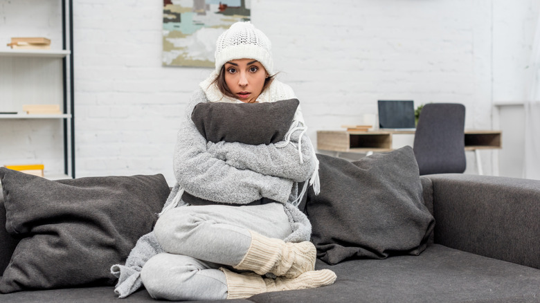 Cold woman wrapped up in blankets sitting on a gray couch