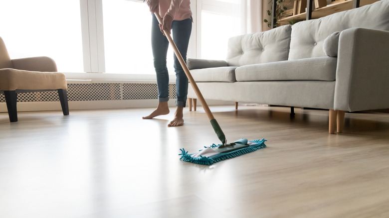 Person sweeping laminate floors next to a couch and chair