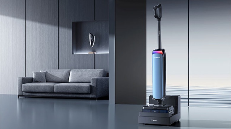 A Tineco FLOOR ONE Station S9 Artist sits in an integrated refresh station charging dock near a gray sofa