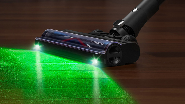 The LightSense headlight of a Tineco PURE ONE A90S illuminates dust particles on a hardwood floor