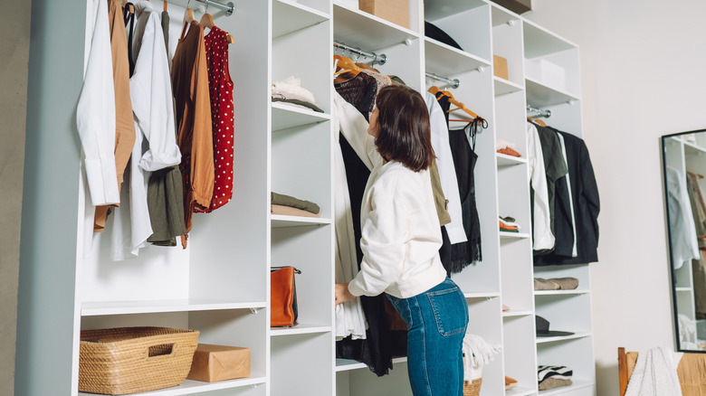 A woman hangs clothes up in the closet.
