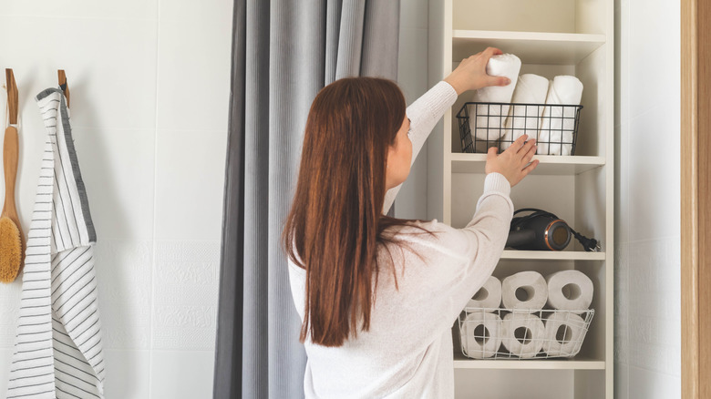 A woman placing towel rolls in a open shelving unit in her bathroom
