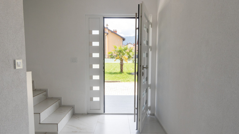 A front door open from inside a house with white walls, floor, and stairs