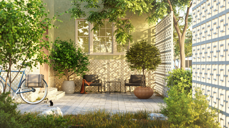 A small patio with trees and plants in pots and a small table and two chairs