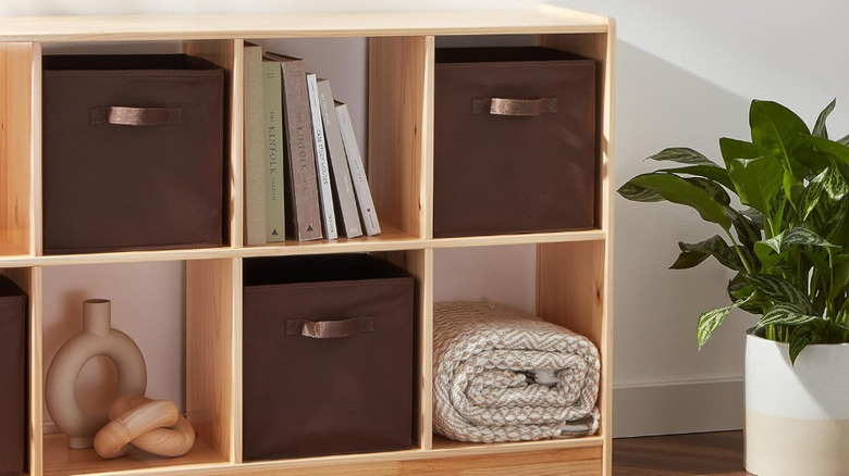 A wood shelf is decorated with vases, book , a blanket and brown fabric organizers.