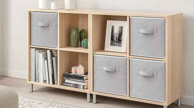 A wooden shelf with  grey storage cubes, stacks of books, and succulents.