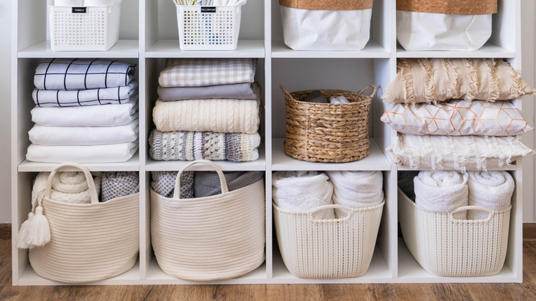 A white shelf with fabric and plastic storage cubes and plants on top