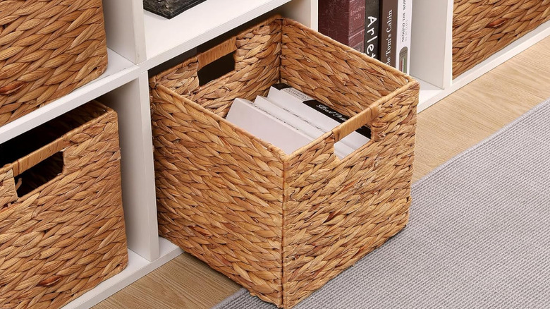 A woven storage cube filled with books is pulled from a white shelf.