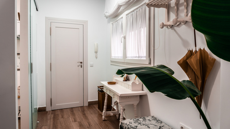 Entryway to a home, with desk used as side table and large potted plant.