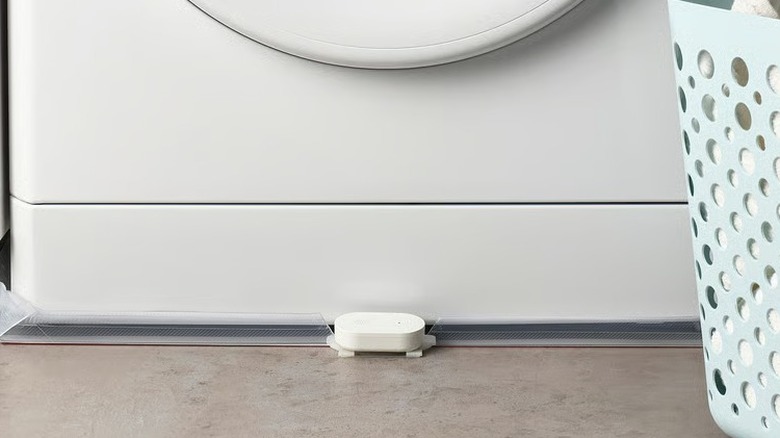 A white water leak sensor placed in front of a washing machine