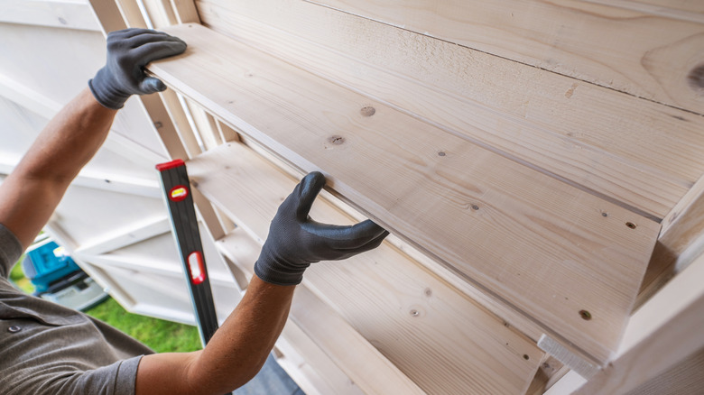 A person installing wooden shelves inside a garden shed