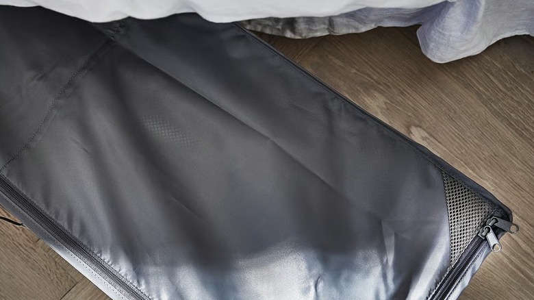 A long dark gray storage case under a bed