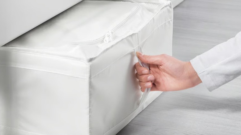 A female hand pulling out a white storage case from under a bed