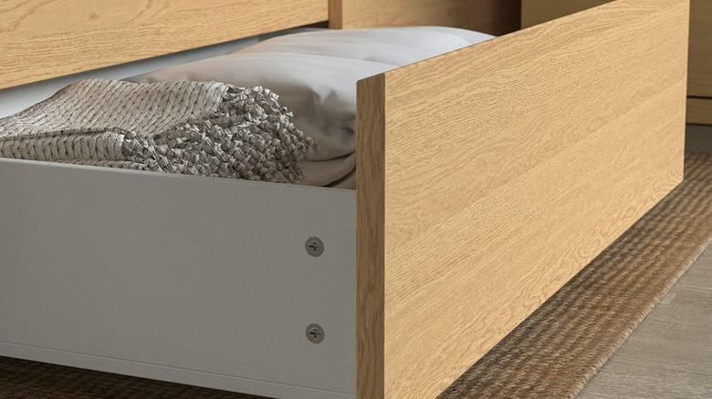 An underbed storage drawer with a wood veneer filled with bedding