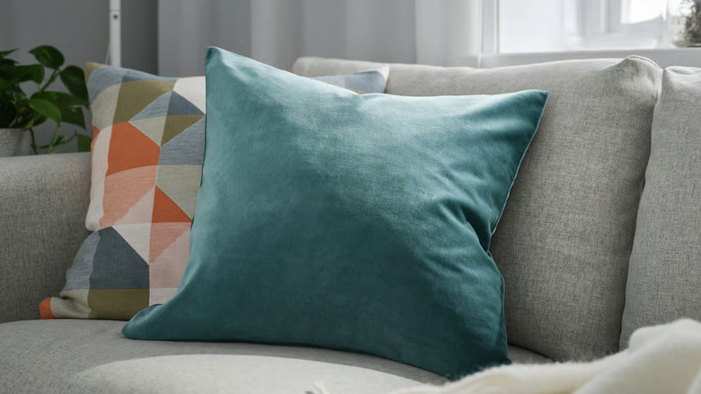 IKEA's SANELA pillow in dark-gray/turquoise velvet on a beige couch