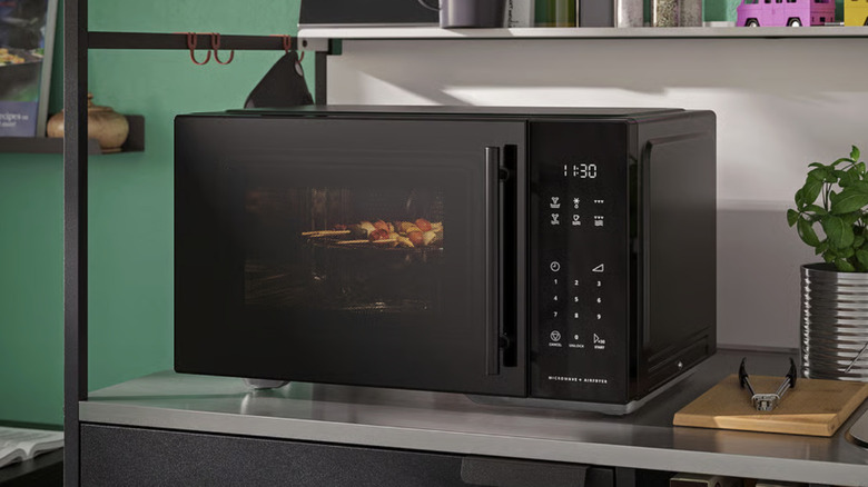 A black microwave oven being used to reheat skewers