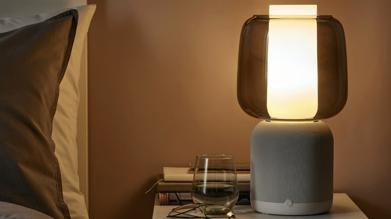 A white speaker lamp with a glass shade on a bedside table