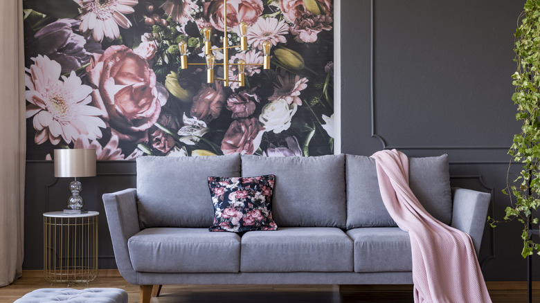 Sofa with flower accent pillow and pink throw blanket in front of floral wallpaper