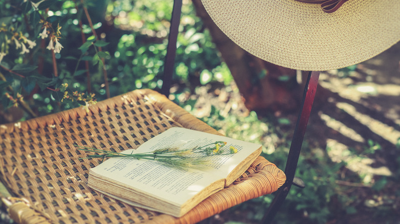 Book with sprig of flowers on a wicker chair with a sunhat in the garden