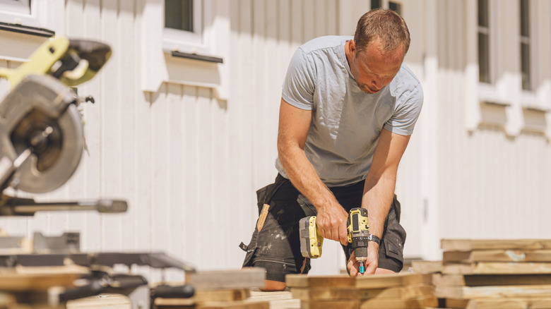 Man using an impact driver drill to install wood decking outside of a home