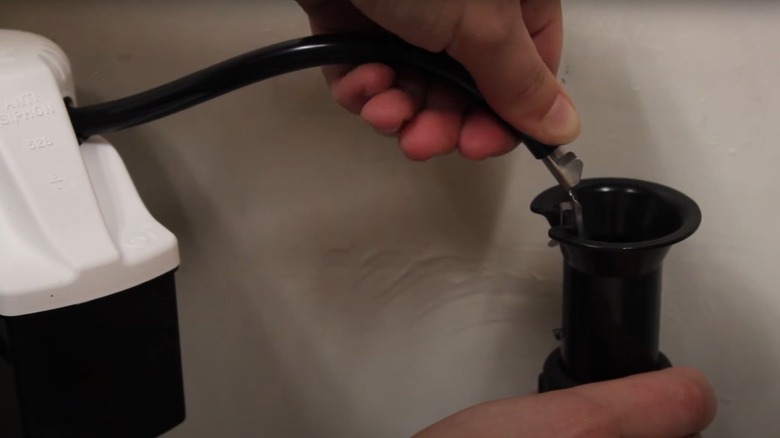 person installing refill tube in toilet