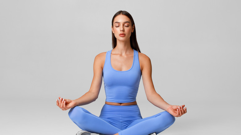 A woman sits in lotus position wearing blue yoga pants and tank top