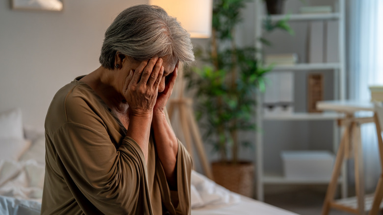Upset woman sitting on the edge of the bed pressing her fingers against her temples.
