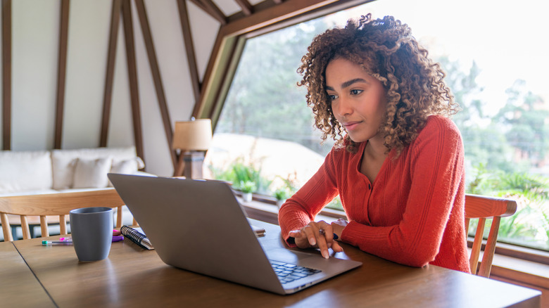 A woman sits at a computer in front of a large window