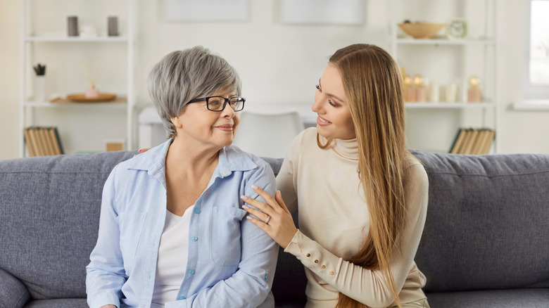 A mother and daughter sit together on a couch having a conversation
