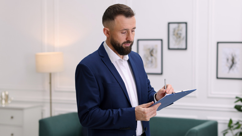 A male appraiser stands in a living room taking notes while touring a home