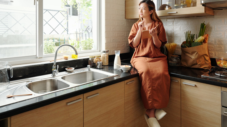 Woman sitting on kitchen counter with a pen and notebook in hand