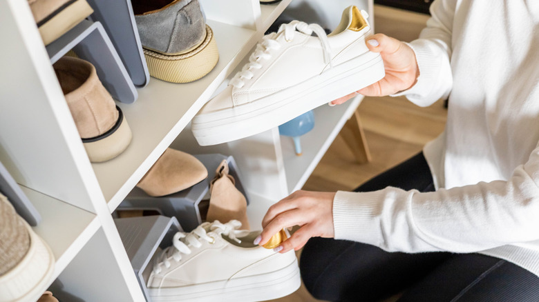 person holding shoes beside storage shelf