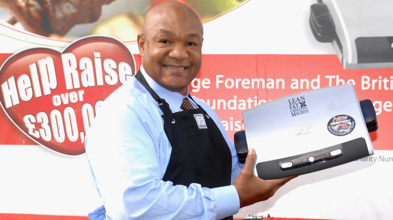 George Foreman smiling and holding up George Foreman Grill at an event