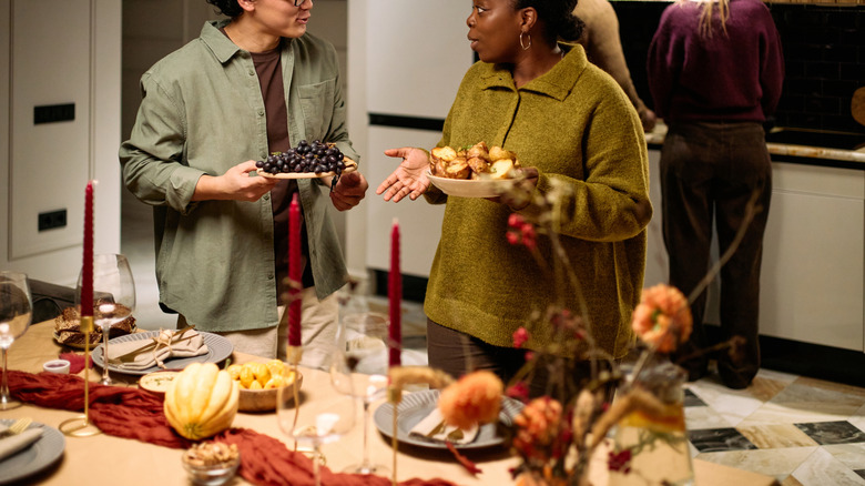 Two people talking while holding plates of food near holiday table